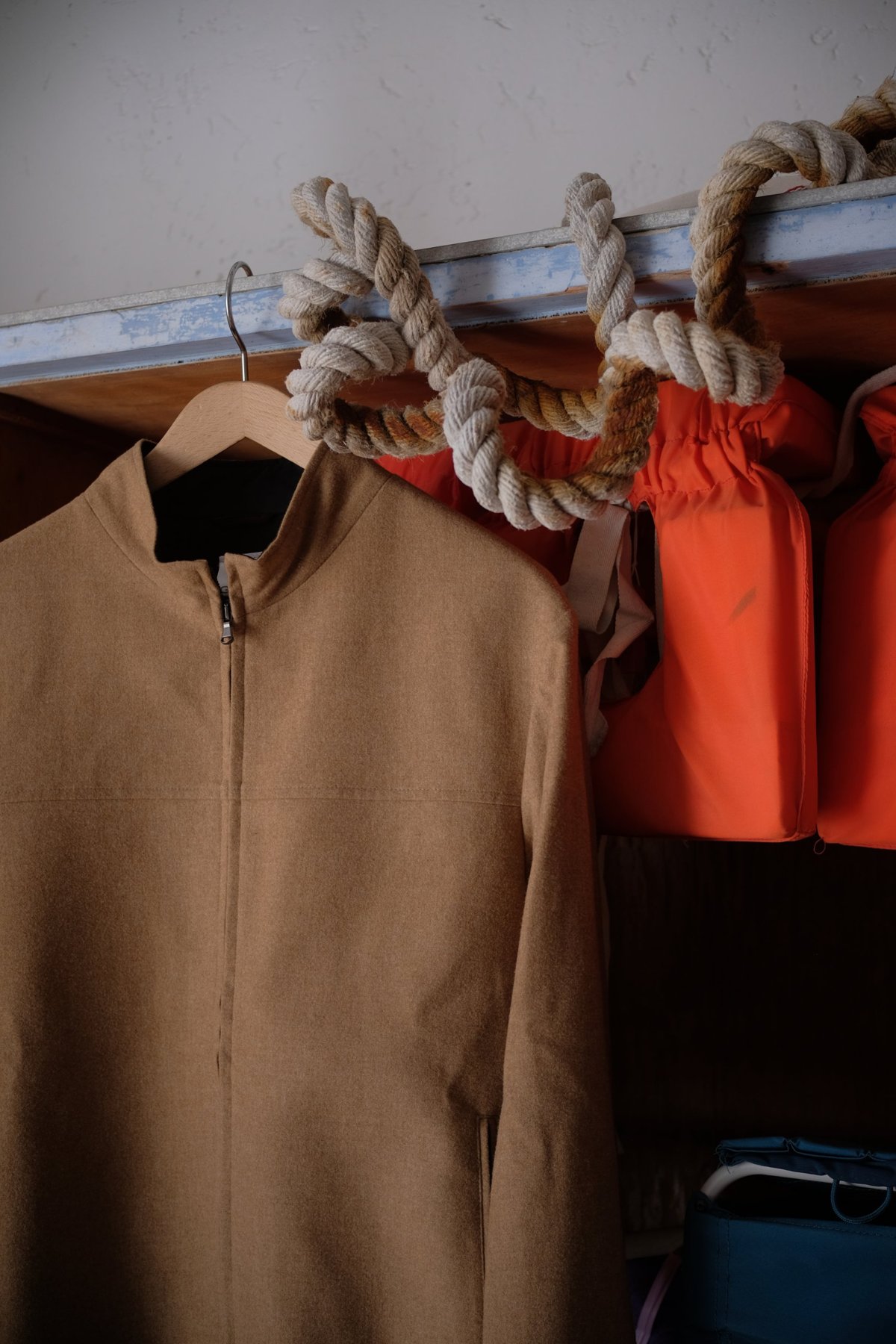 a camel zip jacket on a wooden hanger beside coiled ropes and orange life jackets