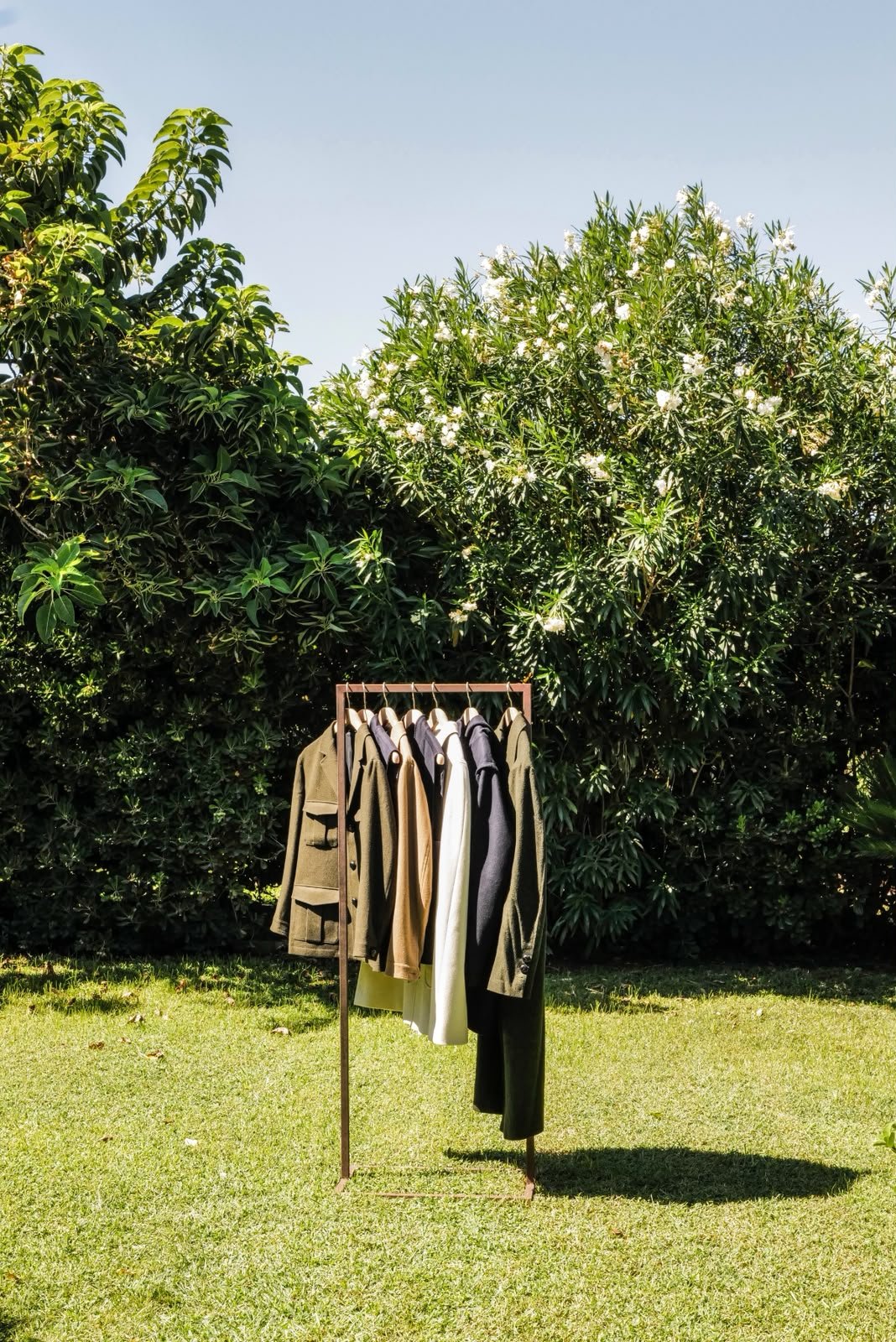 a rail of loden jackets and coats on a lawn in front of flowering bushes