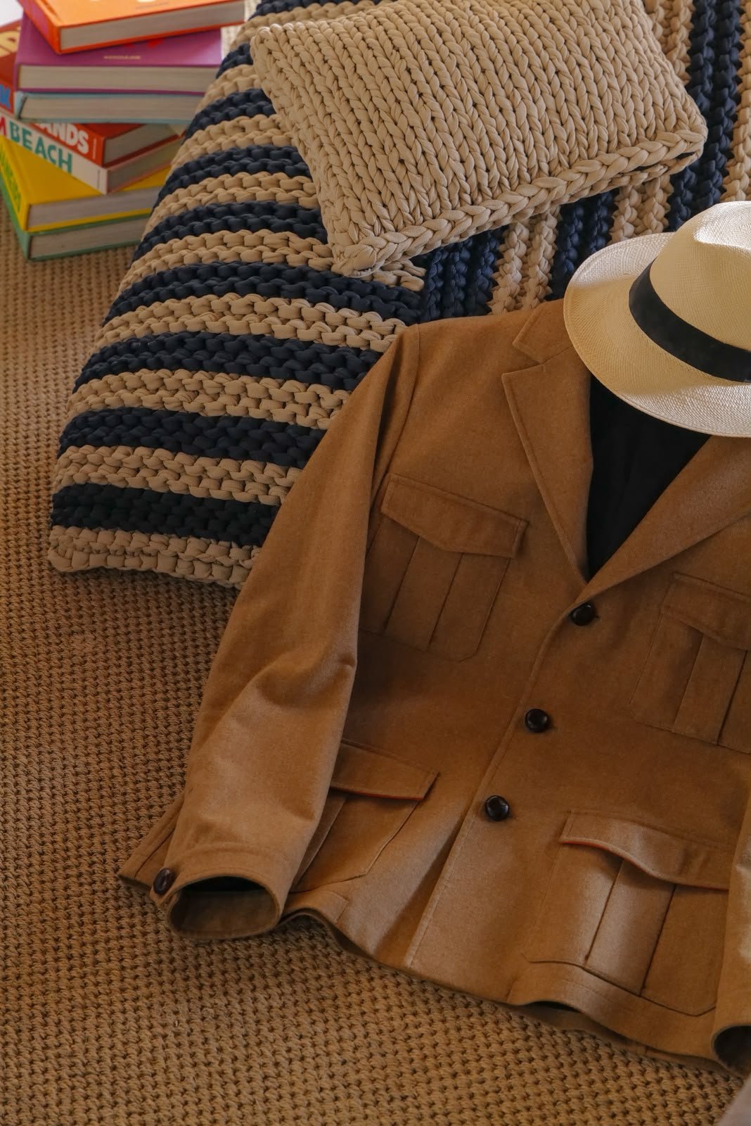 a camel four-pocket jacket on a woven rug beside a straw hat