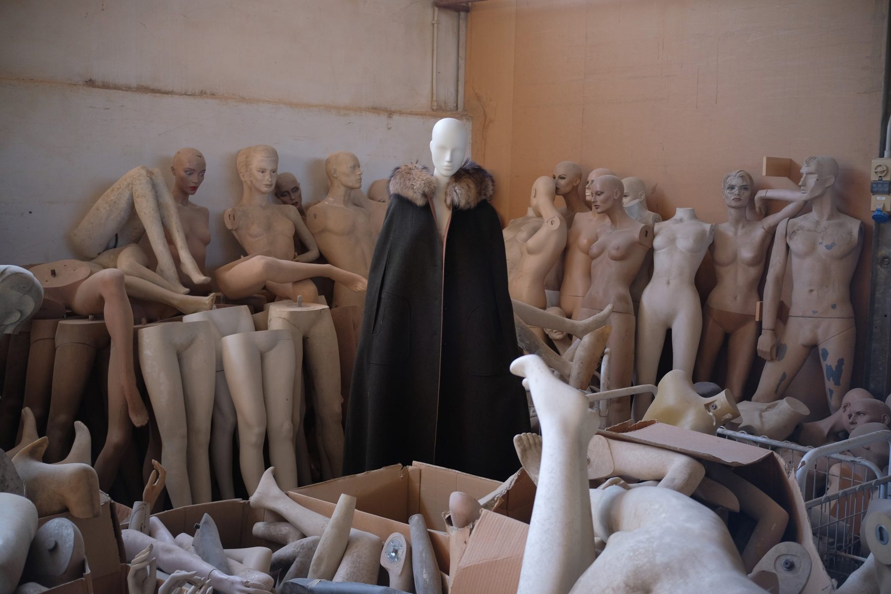 a dark green loden cape with a fur collar among old mannequins